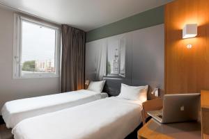 a hotel room with two beds and a laptop on a desk at B&B HOTEL Valenciennes in Marly