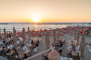 un grupo de personas sentadas en la playa al atardecer en Leonardo Beach Tel Aviv, en Tel Aviv
