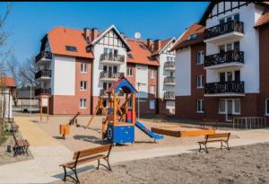 un parque infantil con tobogán y bancos frente a los edificios en Sztutowo Apartament Jaś en Sztutowo