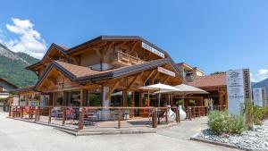 un grand bâtiment en bois avec des tables et des parasols dans l'établissement La Ferme Du Lac, à Thyez