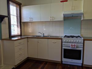 a kitchen with white cabinets and a stove and a sink at Walnut Cottage - 2 bedroom pet friendly country cottage in Bridgetown