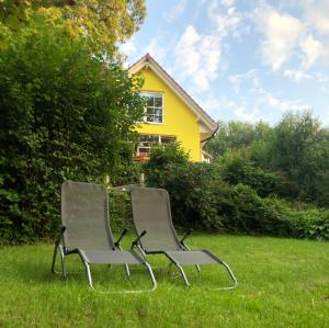 two chairs sitting in the grass in front of a yellow house at Haus am Pinnower See in Pinnow