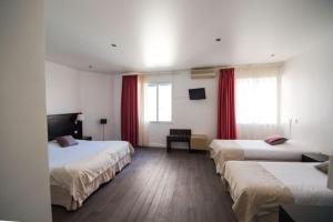 Hôtel Comté de Nice في بوليو سور مير: غرفة فندقية بثلاث اسرة بستائر حمراء
