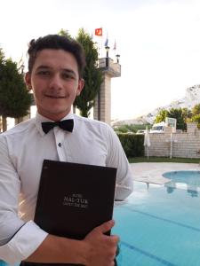 un hombre con corbata de moño sosteniendo un libro en Hotel HAL-TUR, en Pamukkale