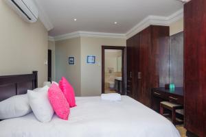 Schlafzimmer mit einem Bett mit rosa Kissen und einem Schreibtisch in der Unterkunft Ballito Manor Beach 405 - FAMILY ONLY - With Generator in Ballito