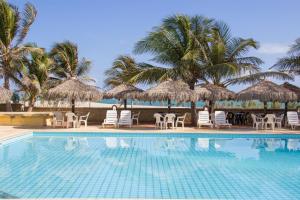a swimming pool with chairs and umbrellas and palm trees at Villa del Mar Praia Hotel in Camocim