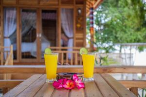 zwei Gläser Orangensaft und Blumen auf einem Holztisch in der Unterkunft Wooden Beach Sunset Cottages in Nusa Lembongan