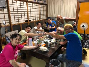 Eine Gruppe von Menschen, die an einem Tisch sitzen und Essen essen. in der Unterkunft Rider & Guest House Kazeyoubi in Fukuyama