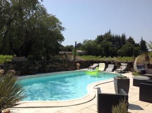 a swimming pool with chairs and a stone wall at Gîte la Genestière in Sérignan-du-Comtat