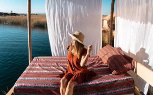 a woman in a hat sitting on a bed next to the water at Uros Caminos del Titicaca Peru in Puno