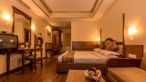 a hotel room with a bed and a desk and a television at Hotel Nahar Nilgiris in Ooty