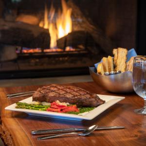 a steak on a plate on a table with a fireplace at Chautauqua Harbor Hotel - Jamestown in Celoron