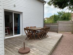 Maison récente à 200m de la plage في Bernières-sur-Mer: سطح خشبي مع طاولة وكراسي خشبية