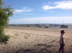 un joven parado en una playa con barcos en el agua en Appart Terrasse Végétale bord Plages bassin en Arès