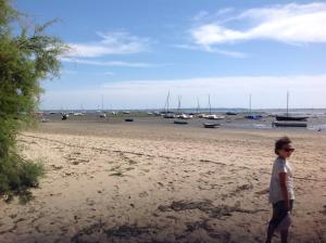 a young boy standing on a beach with boats in the water at Appart Terrasse Végétale bord Plages bassin in Arès +4 photos
