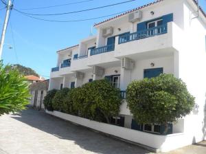 ein weißes Gebäude mit blauen Balkonen auf einer Straße in der Unterkunft Ostria Eressos Rooms in Skala Eresou