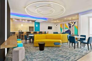 a lobby with a yellow couch and tables and chairs at La Quinta by Wyndham Richmond-Sugarland in Richmond