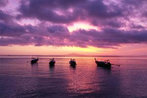 three boats sitting in the water at sunset at Phi Phi Relax Beach Resort in Phi Phi Islands +37 photos
