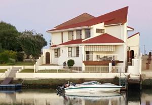 a boat sitting in front of a house on the water at Port Owen Self Catering in Velddrif