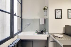 La salle de bains est pourvue d'un lavabo blanc et d'une fenêtre. dans l'établissement Sous Le Cèdre - Au cœur de Nantes, à Nantes