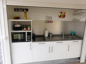 a kitchen with white cabinets and a microwave and a sink at Perle de Clugny in Sainte-Rose