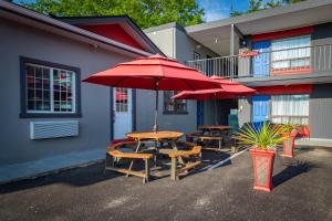 deux tables et chaises avec parasols rouges devant un bâtiment dans l'établissement Villager Lodge Niagara Falls, à Niagara Falls