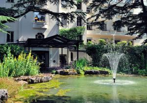 une fontaine dans un étang en face d'un bâtiment dans l'établissement Le Grand Hôtel - Domaine De Divonne, à Divonne-les-Bains