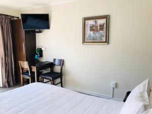 Habitación de hotel con cama, escritorio y TV. en Tudor Court Motor Lodge en Auckland