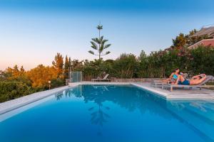 - deux femmes assises sur des chaises à côté d'une piscine dans l'établissement Villa OMNIA - Kommeno bay, à Dassia