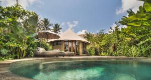 a swimming pool in front of a house at Sandat Glamping Tents in Ubud