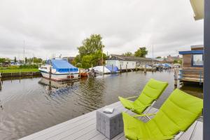 a dock with two chairs and a boat in the water at Bright and Comfortable Houseboat in Aalsmeer