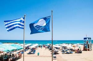 Dos banderas en una playa con sillas y sombrillas. en Oasis Studio, en Kokkíni Khánion