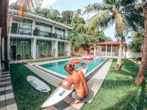 a man sitting next to a swimming pool with a surfboard at Green Hill Mirissa in Mirissa