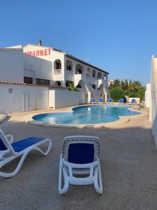 a pair of lounge chairs and a pool in front of a hotel at Apartamentos Xoroi in Cala en Porter