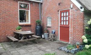 uma mesa de piquenique em frente a um edifício de tijolos com uma porta vermelha em Riley's cottage em Hemrik