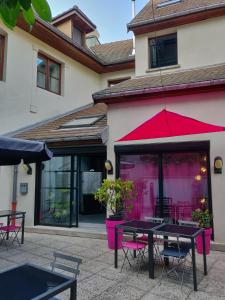 een patio met tafels en stoelen en een rode parasol bij Hôtel Le Lacuzon in Moirans-en-Montagne
