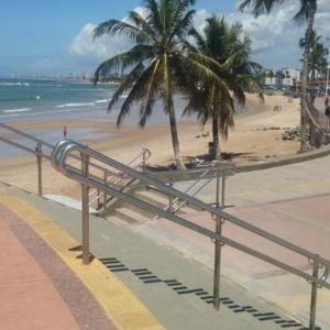 a beach with palm trees and a metal hand rail at Kitnets com AR Condicionado na Praia in Salvador