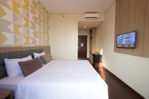 Cette chambre comprend un lit blanc et une télévision murale. dans l'établissement Hotel 88 ITC Fatmawati Jakarta By WH, à Jakarta