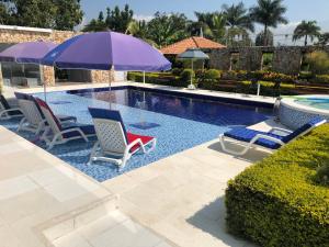 Rozo的住宿－La Morocha Hospedaje & Relax Campestre，一个带两把椅子和紫色遮阳伞的游泳池