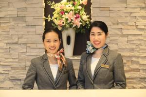 two women in suits standing next to a wall with flowers at Richmond Hotel Namba Daikokucho in Osaka