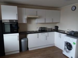 a kitchen with white cabinets and a washer and dryer at Panoramic Harbour View Apartment in Oban
