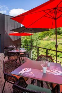 a patio with tables and red umbrellas on a deck at Hôtel & Restaurant Sodade in Chaudes-Aigues