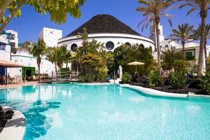 a swimming pool in front of a building with palm trees at Hotel LIVVO Volcán Lanzarote in Playa Blanca