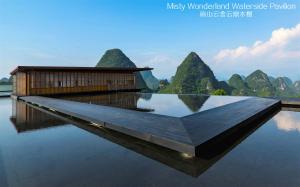un edificio sull'acqua con montagne sullo sfondo di Misty Wonderland ,Yangshuo Xingping a Yangshuo