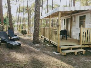 eine Holzhütte mit einer Veranda und Stühlen neben einem Baum in der Unterkunft Mobilhome tout confort - Les dunes de Contis in Saint-Julien-en-Born