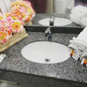 a bathroom counter with a white sink and flowers at Pousada Gardenia Guest House in Gramado