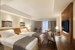 a hotel room with two beds and a desk and a television at Windsor Marapendi Hotel in Rio de Janeiro