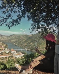 Una donna seduta su una collina con un bicchiere di vino di Dois Lagares House a Pinhão