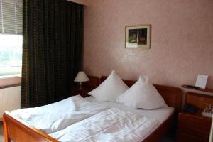 a bedroom with a bed with white sheets and pillows at Wiking Hotel in Henstedt-Ulzburg