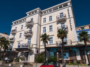 a white building with palm trees in front of it at Hotel Galeb in Opatija